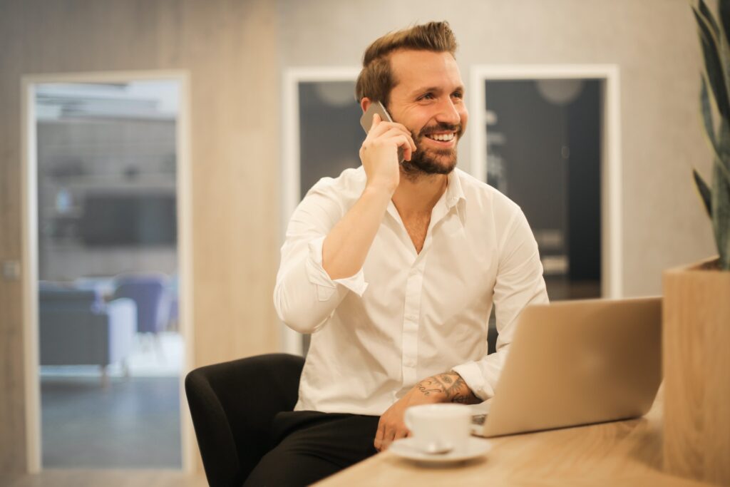 man sitting at desk with macbook talking on the phone and smiling