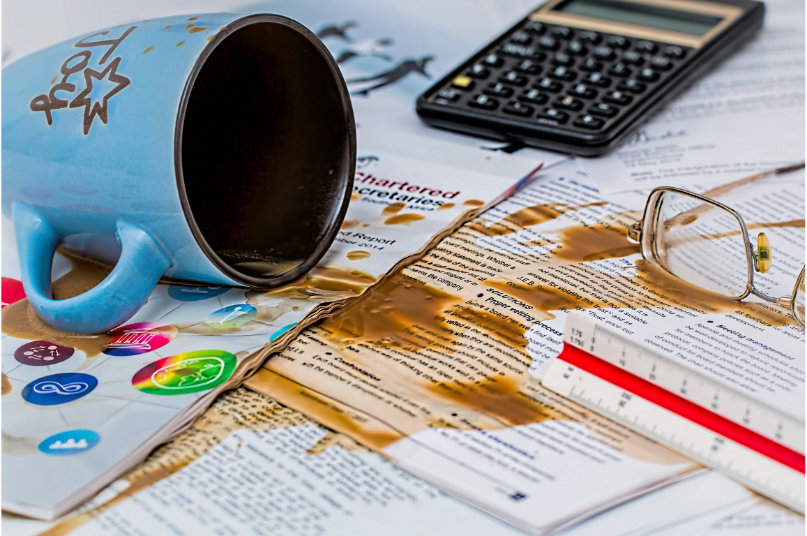 Coffee spilled on messy desk with paperwork calculator and glasses