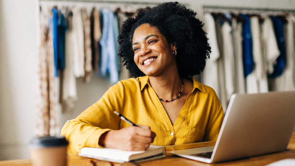 woman smiling in front of laptop with a notebook